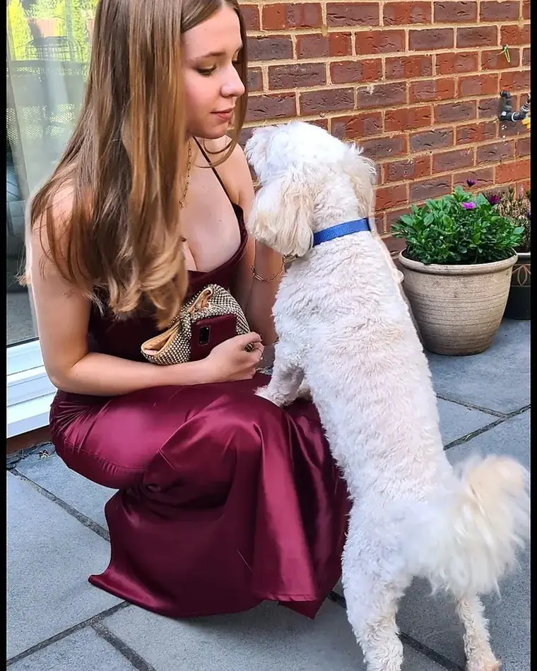 Beth crouching on a patio beside her white miniature poodle, Baloo.