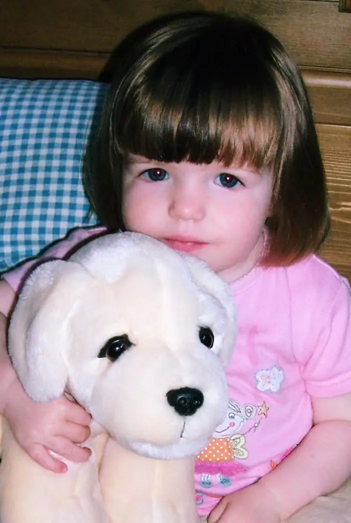 Childhood photograph of a toddler hugging a white toy dog.