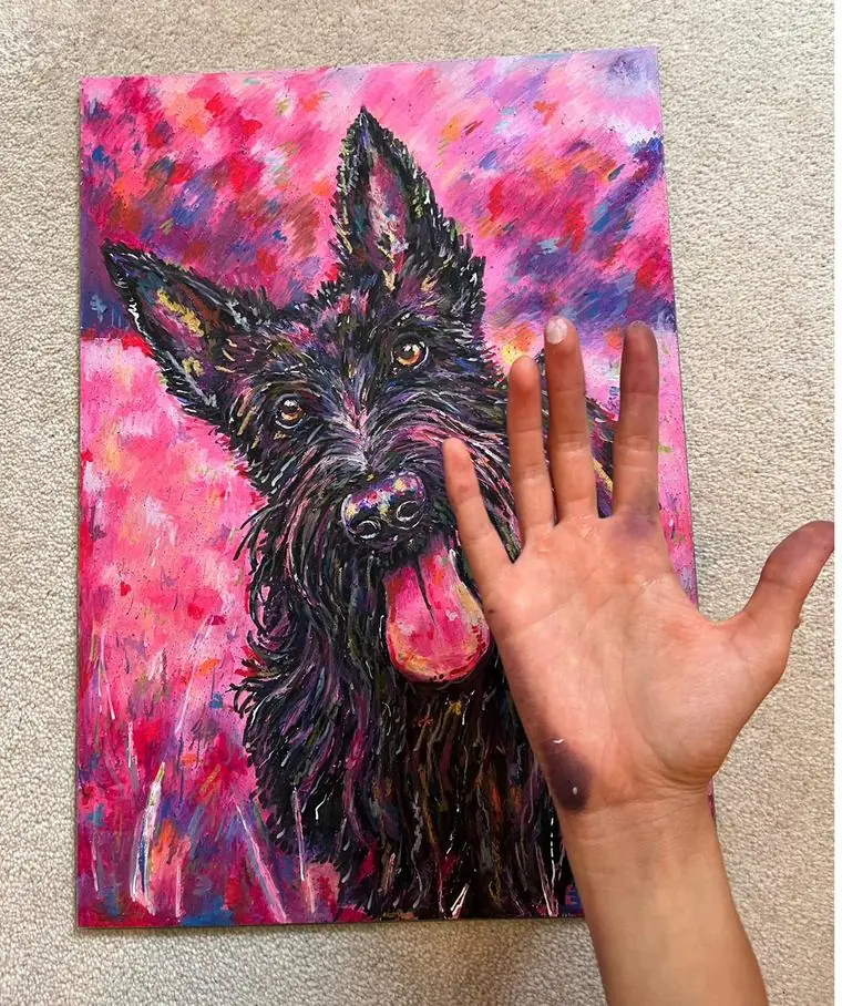 A hand laid on an A3 portrait of a black Scottish terrier to show the size.